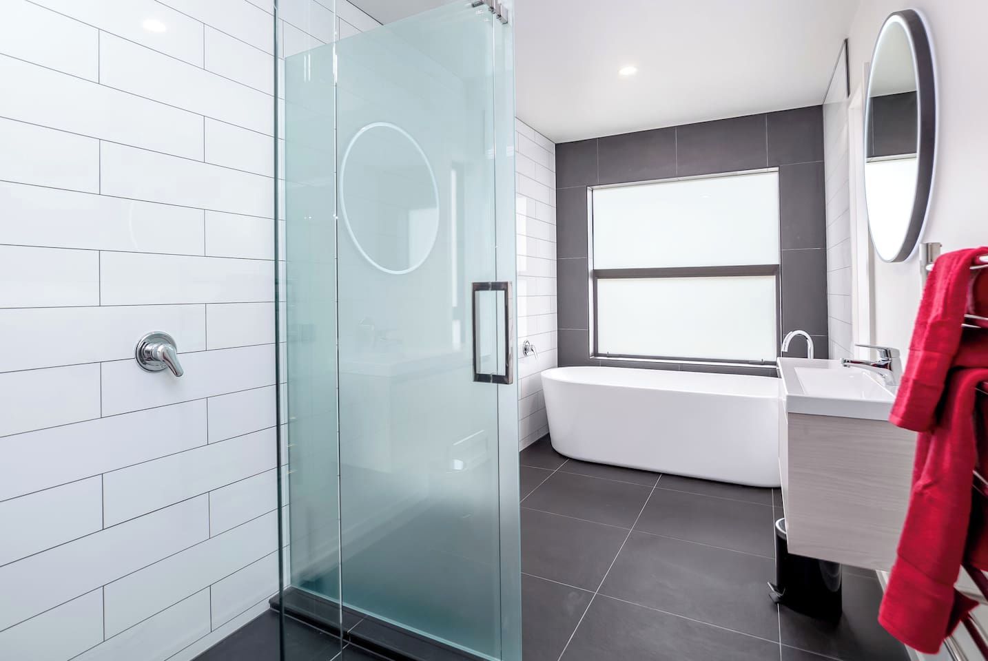 A modern bathroom with a glass shower enclosure, a bathtub, and a large mirror.
