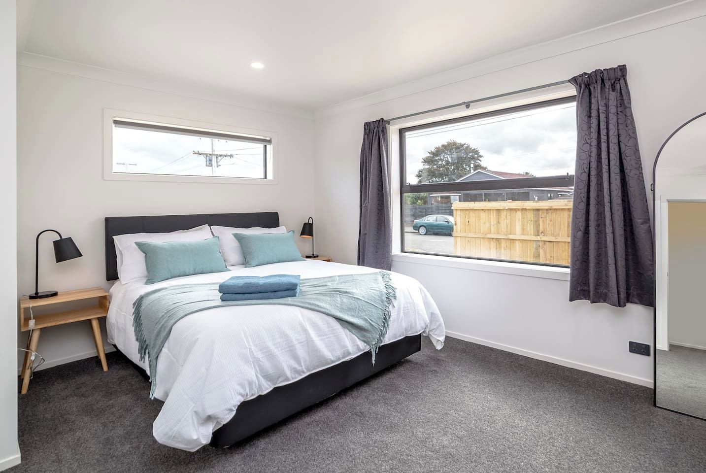 A bedroom with a bed, bedside tables, a window with curtains, and a view of the outside.