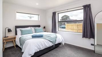 A bedroom with a bed, bedside tables, a window with curtains, and a view of the outside.