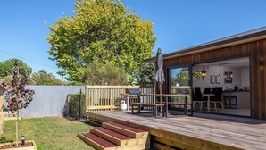 A deck with outdoor seating, a barbecue grill, and a view into a modern kitchen. - Broadway On New York (Martinborough)
