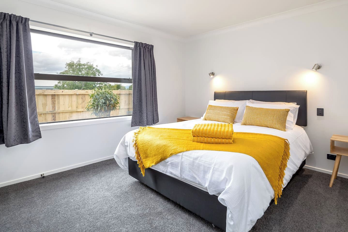 Une chambre à coucher avec un grand lit, une fenêtre avec des rideaux, une table de chevet et une commode.
