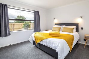 A bedroom with a large bed, a window with curtains, a bedside table, and a nightstand.