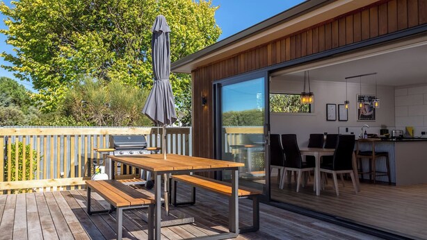 An outdoor deck with a wooden table and benches, a barbecue grill, and a large umbrella. - Broadway On New York (Martinborough)
