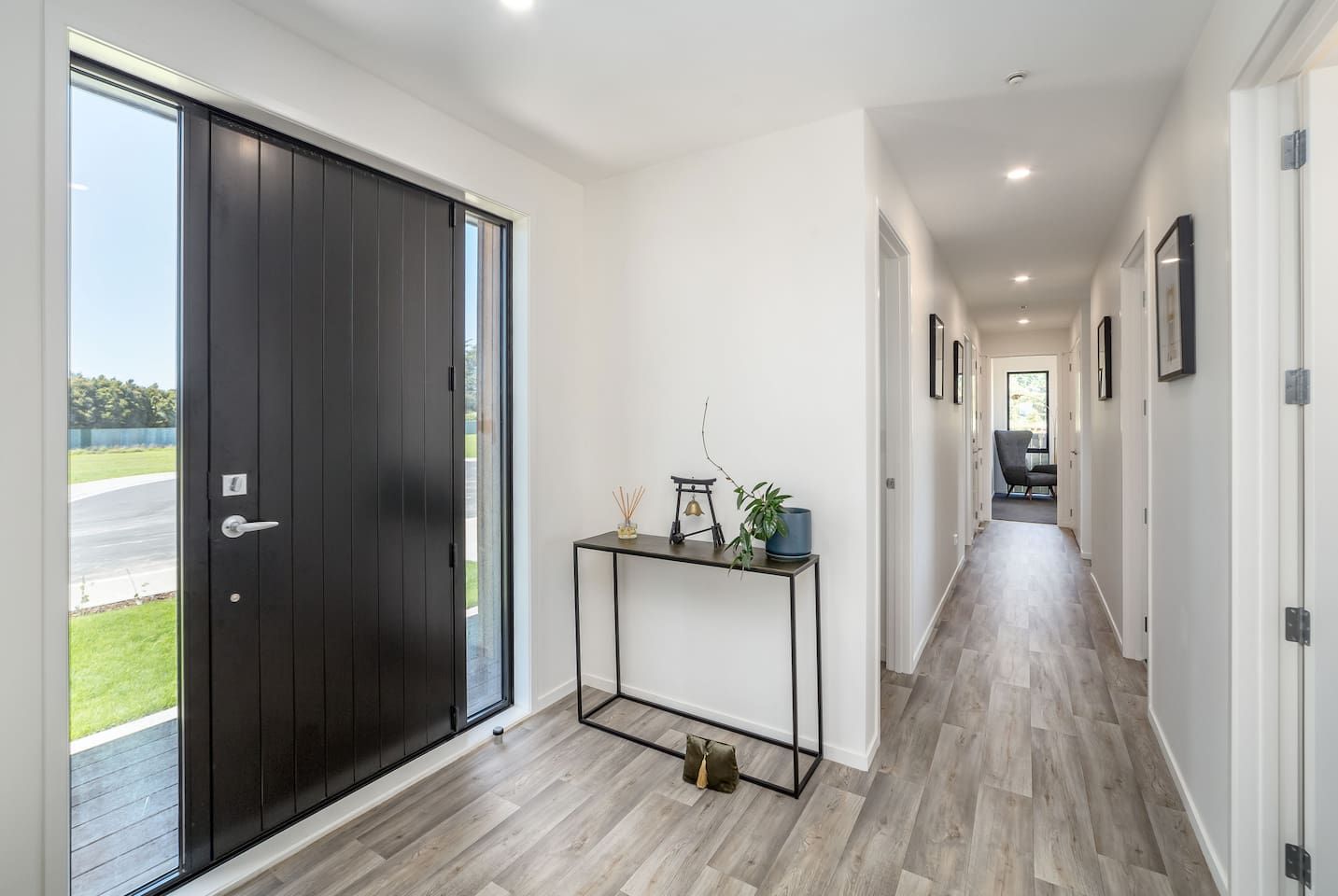 Un pasillo con una puerta de madera oscura, una pequeña consola decorativa y vistas de un paisaje verde a través de la puerta.