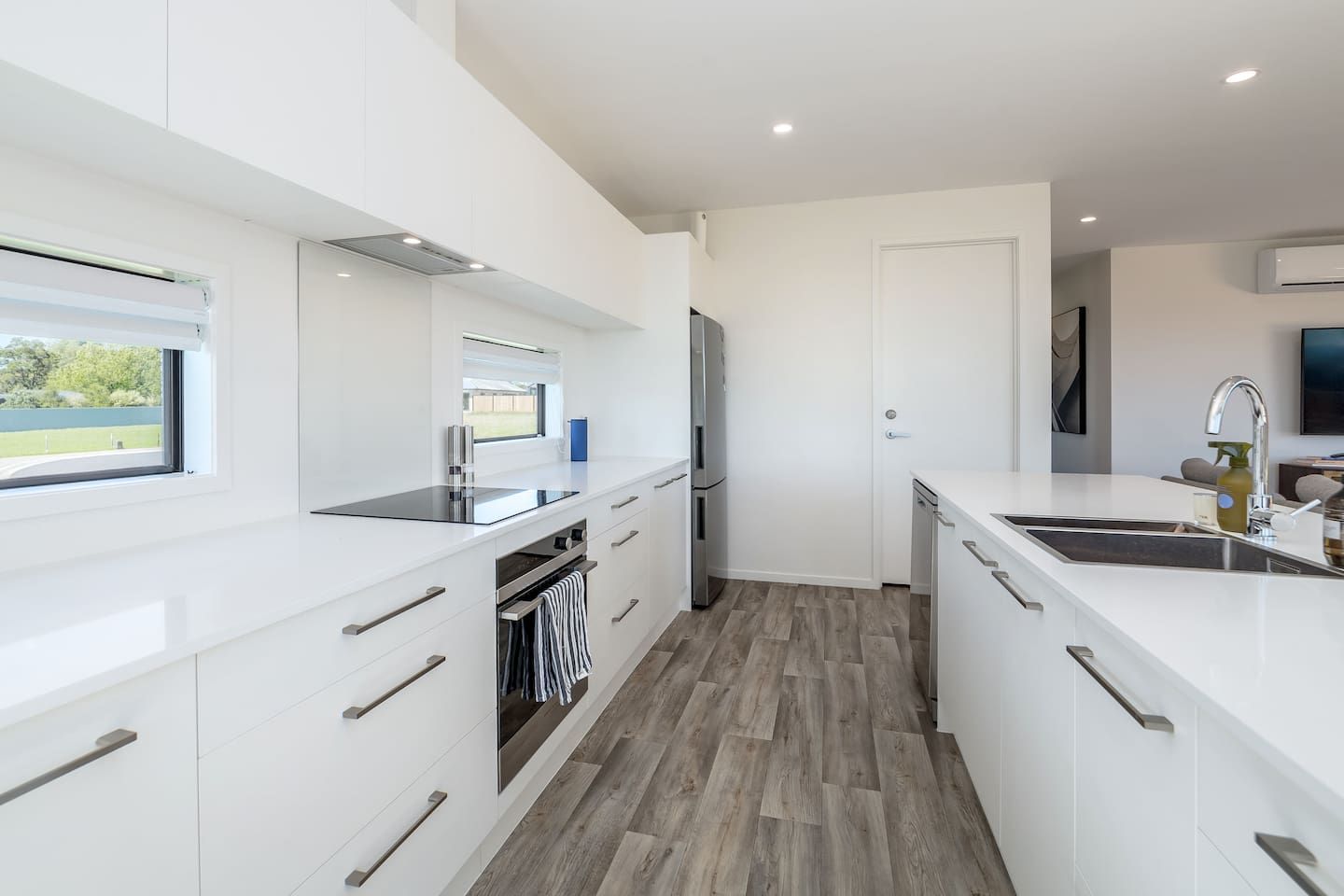 Una cocina moderna con armarios blancos, horno empotrado y ventana con vistas a un paisaje verde.