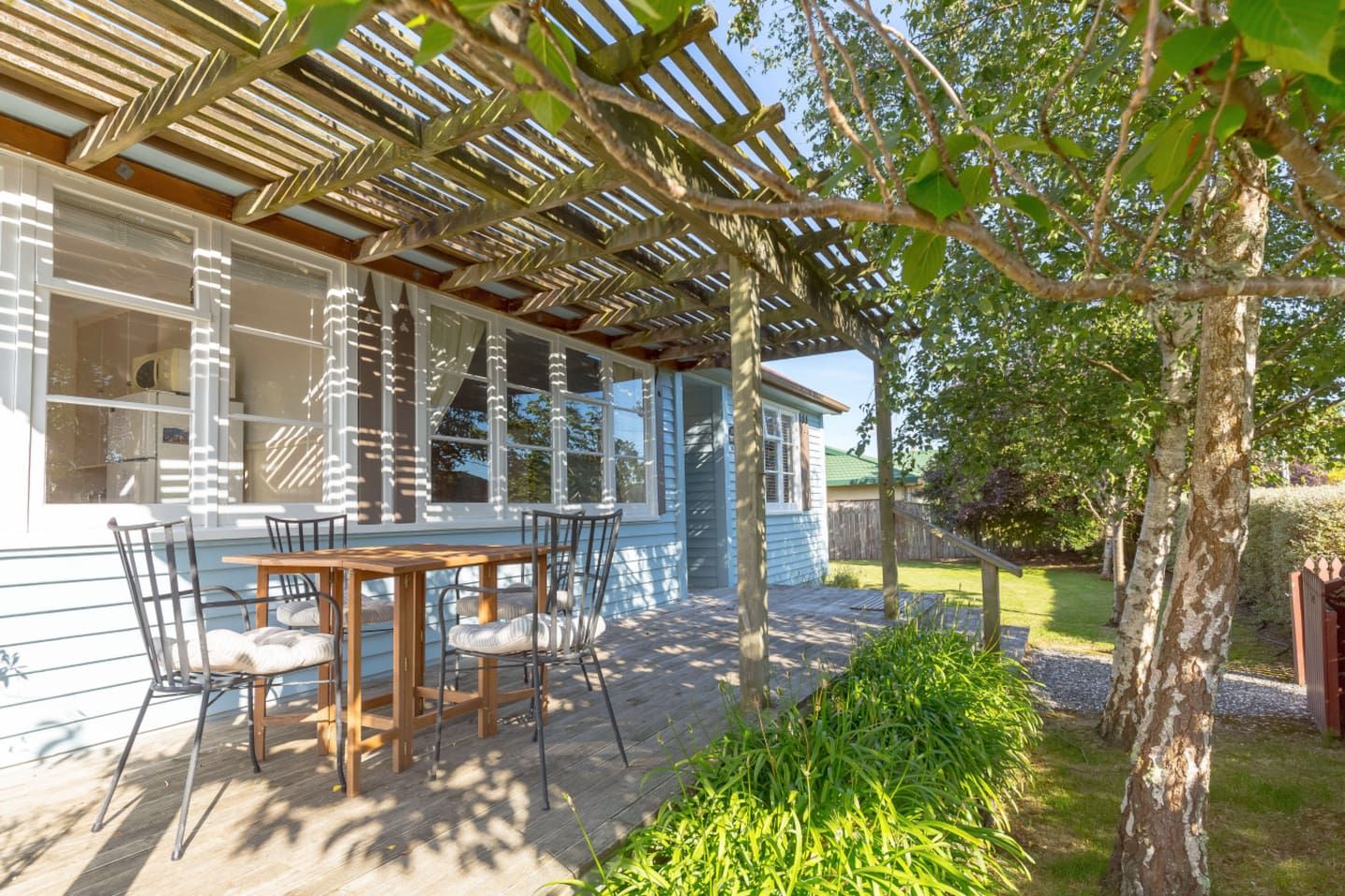 A covered patio with a table and chairs, a pergola overhead, and a view of a house with a window.