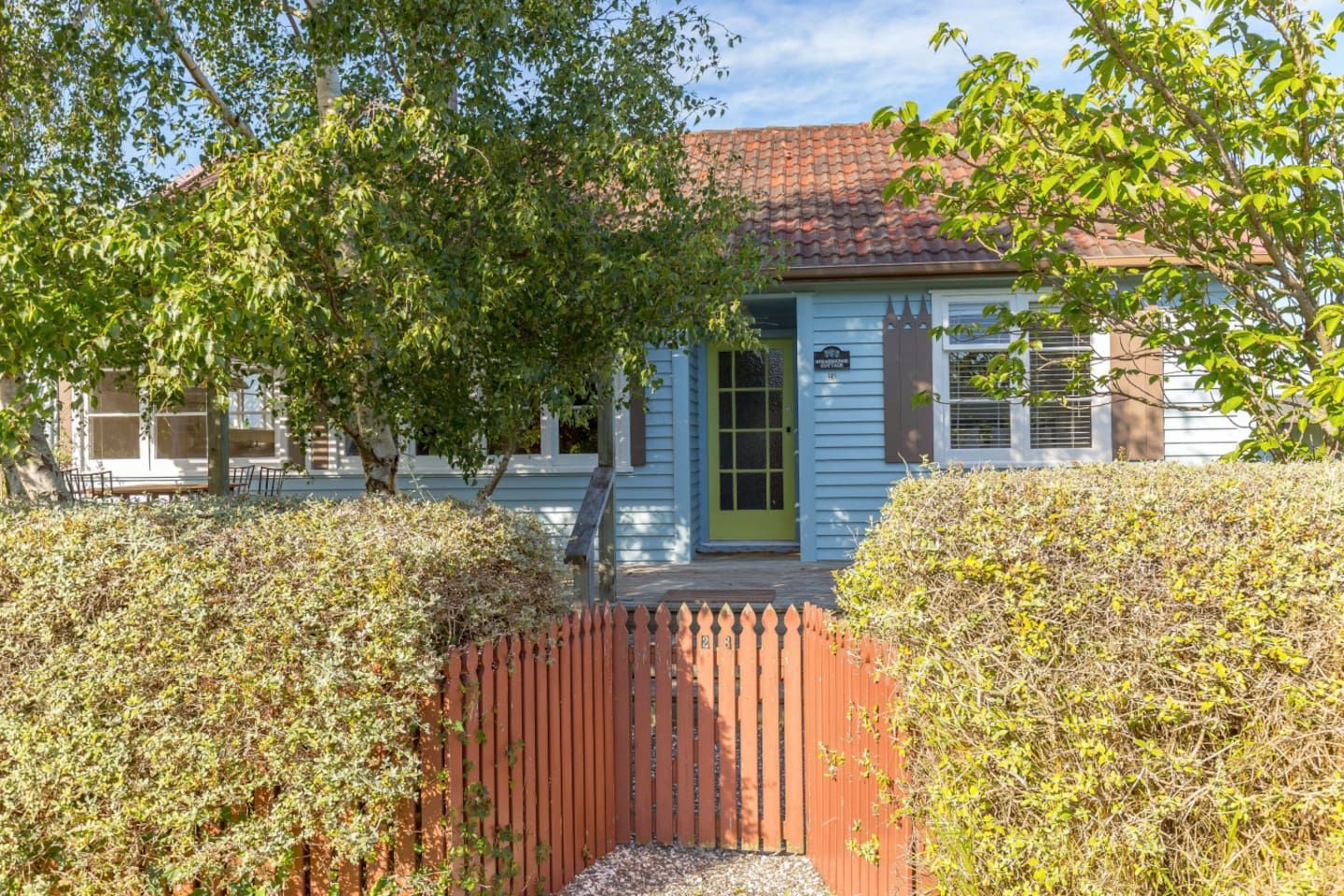 Une maison à deux étages avec une porte verte et une clôture en bois peinte en rouge.