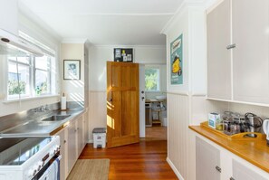 A kitchen with a wooden door, stainless steel appliances, and a view into the adjacent room. - Strasbourge Cottage, Martinborough (Martinborough)