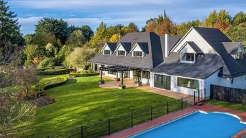 A modern two-story house with a large backyard, a swimming pool, and a well-maintained garden.
