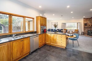 A modern kitchen with wooden cabinets, a dishwasher, and a dining area with a brick fireplace. - Longbush Estate, Gladstone (Longbush)