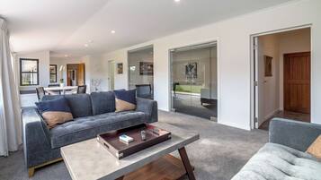 A modern living room with a grey sofa, a coffee table, and a view of the backyard through glass doors.