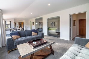 A modern living room with a grey sofa, a coffee table, and a view of the backyard through glass doors. - Longbush Estate, Gladstone (Longbush)