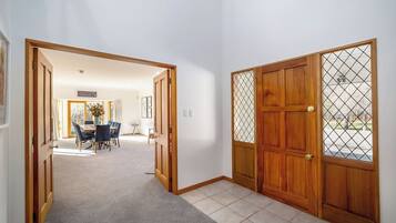 A hallway with a carpeted floor, wooden doors, and a dining area with chairs and a table.