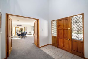 A hallway with a carpeted floor, wooden doors, and a dining area with chairs and a table. - Longbush Estate, Gladstone (Longbush)