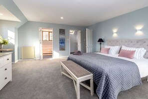 A bedroom with a bed, bedside table, and a bench. There is a door leading to another room, a radiator, and a wall-mounted light fixture.
