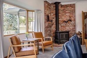 A room with a brick fireplace, a table with chairs, and a window with curtains. - Longbush Estate, Gladstone (Longbush)