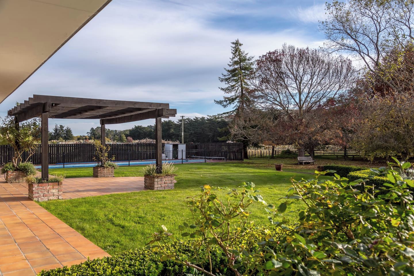 Un área de patio techada con piscina, rodeada por un patio cercado y árboles.