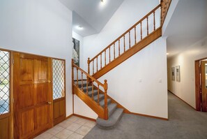 A wooden staircase with a carpeted landing, a wooden door with glass panels, and a hallway with framed pictures. - Longbush Estate, Gladstone (Longbush)