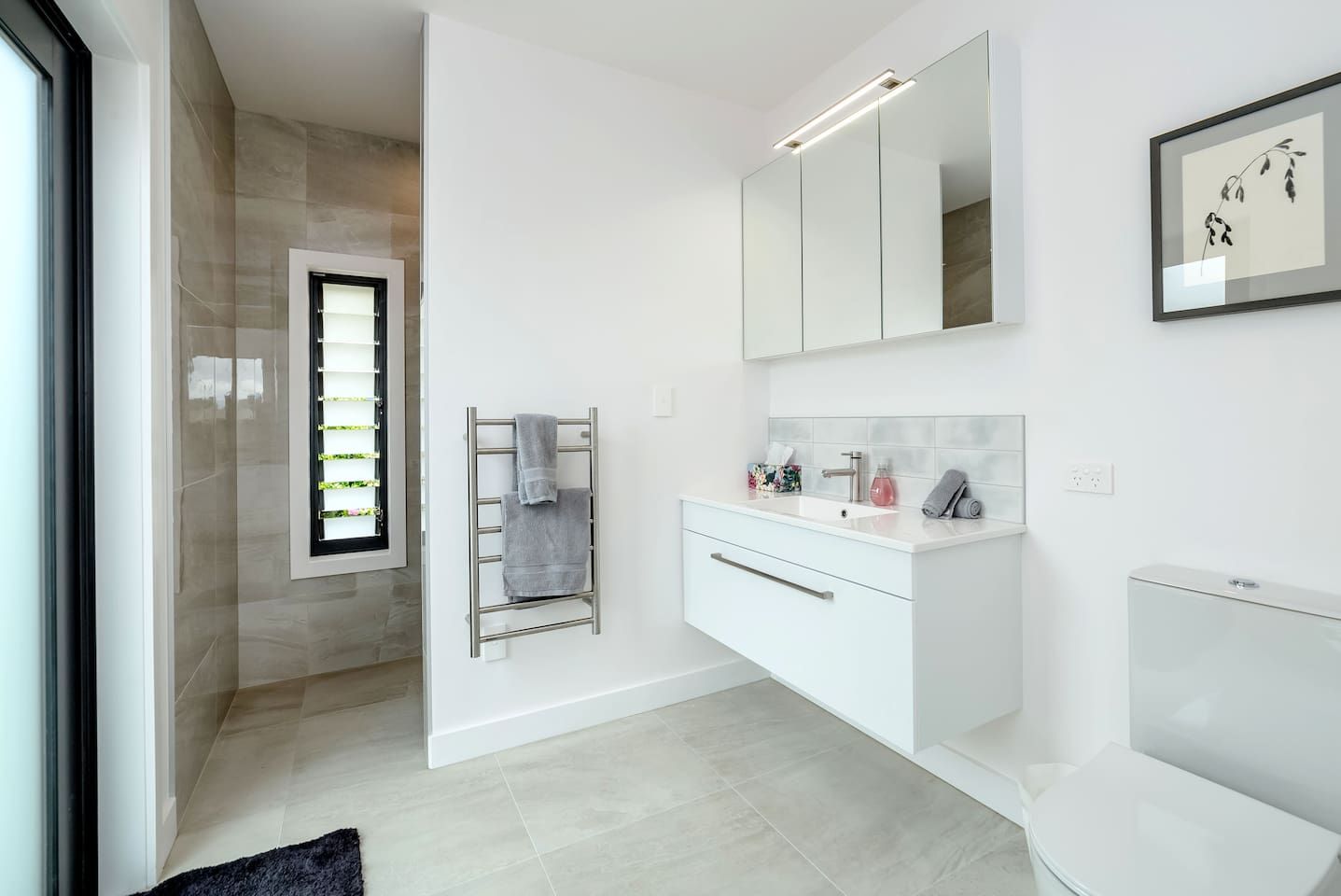 A modern bathroom with a glass shower enclosure, a white vanity with a mirror, and a towel rack.
