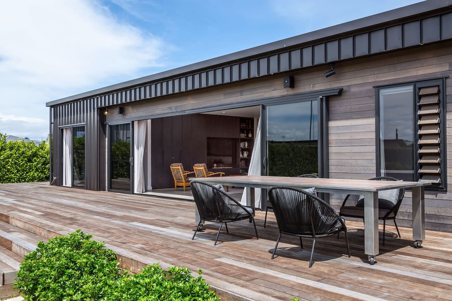 A modern house with a wooden deck, outdoor seating, and large windows.