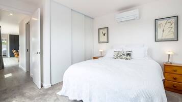 A bedroom with a large bed, a nightstand, a dresser, and a door leading to another room.