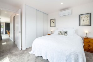 A bedroom with a large bed, a nightstand, a dresser, and a door leading to another room.