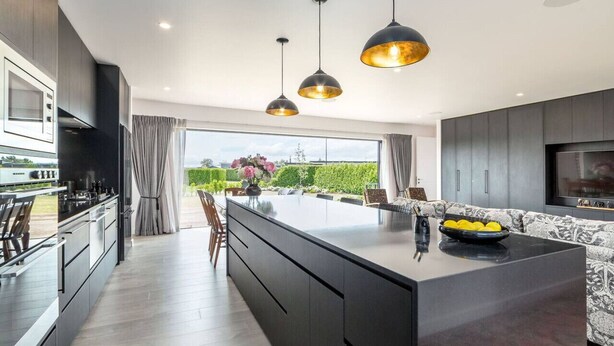 Uma cozinha moderna com armários escuros, uma ilha central e iluminação pendente.