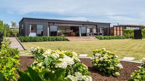 Une maison moderne à deux étages, dotée d’un patio couvert, d’un jardin agrémenté d’hortensias et d’une terrasse en bois.