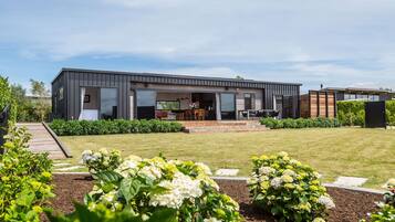 A modern two-story house with a covered patio, a garden with hydrangeas, and a wooden deck.