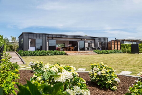 A modern two-story house with a covered patio, a garden with hydrangeas, and a wooden deck.