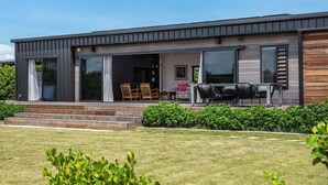Une maison moderne à deux étages, dotée d’un patio couvert, d’un coin repas avec mobilier d’extérieur et d’une pelouse bien entretenue.