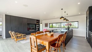 Cozinha moderna com área de refeições, destacando uma grande mesa de madeira, cadeiras e TV embutida.