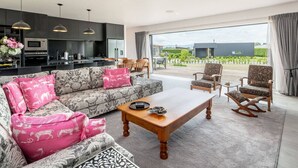 Uma sala de estar moderna com sofá, mesa de centro e cadeiras, área de cozinha com eletrodomésticos e uma grande janela com vista para o exterior.