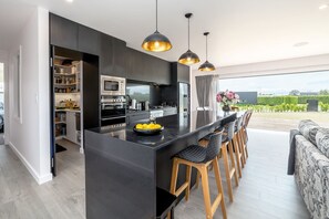 A modern kitchen with a central island, bar stools, and a dining area with a view. - Relax on the Deck, Martinborough (Martinborough)
