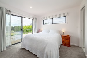 A bedroom with a large bed, a nightstand, a window, and a view of a green landscape.