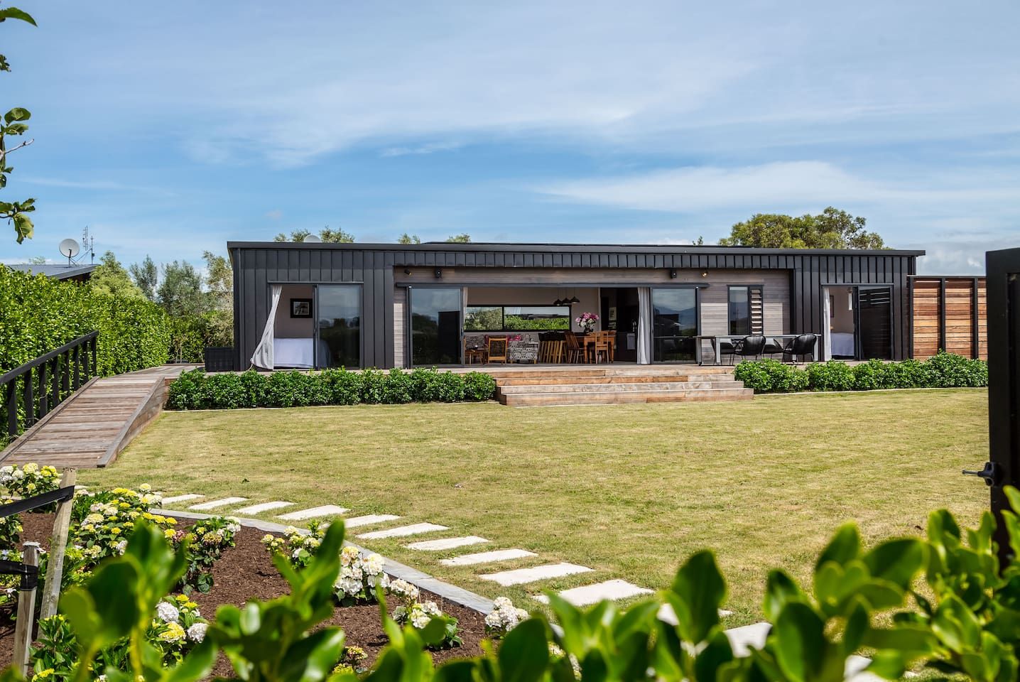 A modern two-story house with a covered patio, a wooden deck, and a well-maintained lawn.