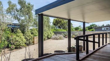 A covered outdoor deck with a wooden floor and black railings, surrounded by a garden with various plants and a gravel area.
