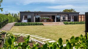 Uma casa moderna de dois andares com um alpendre coberto, um deck de madeira e um gramado bem cuidado.