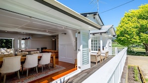 A modern house with an open-plan kitchen and dining area, a wooden deck, and a view of a green landscape.