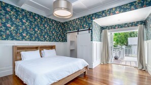 A bedroom with a wooden bed, floral wallpaper, a ceiling light, and a view of the outdoors.