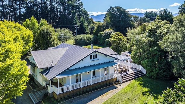 A two-story house with a balcony and a deck, surrounded by lush greenery and trees.