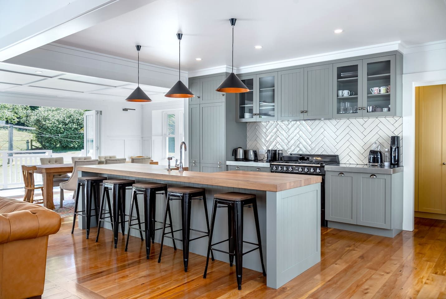 Cozinha moderna com ilha central, banquetas, iluminação pendente e painel de azulejos em padrão herringbone.