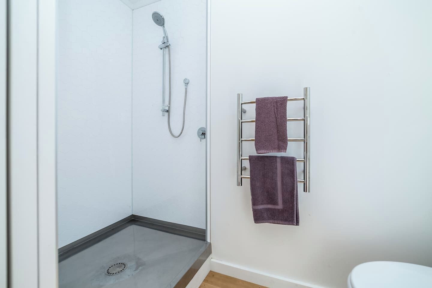 A bathroom with a shower, a towel rack with two towels, and a toilet.