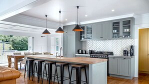 A modern kitchen with grey cabinets, a central island with stools, a herringbone backsplash, and pendant lighting. - The Forest House, Martinborough (Pirinoa)