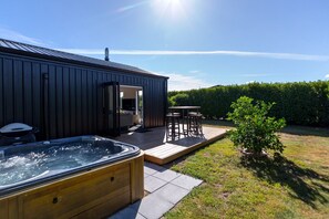 A modern outdoor hot tub area with a wooden deck, a barbecue grill, and a seating arrangement. - Relaxing Martinborough Escape | Spa, Seasonal Communal Pool & Indoor-Outdoor Living (Martinborough)