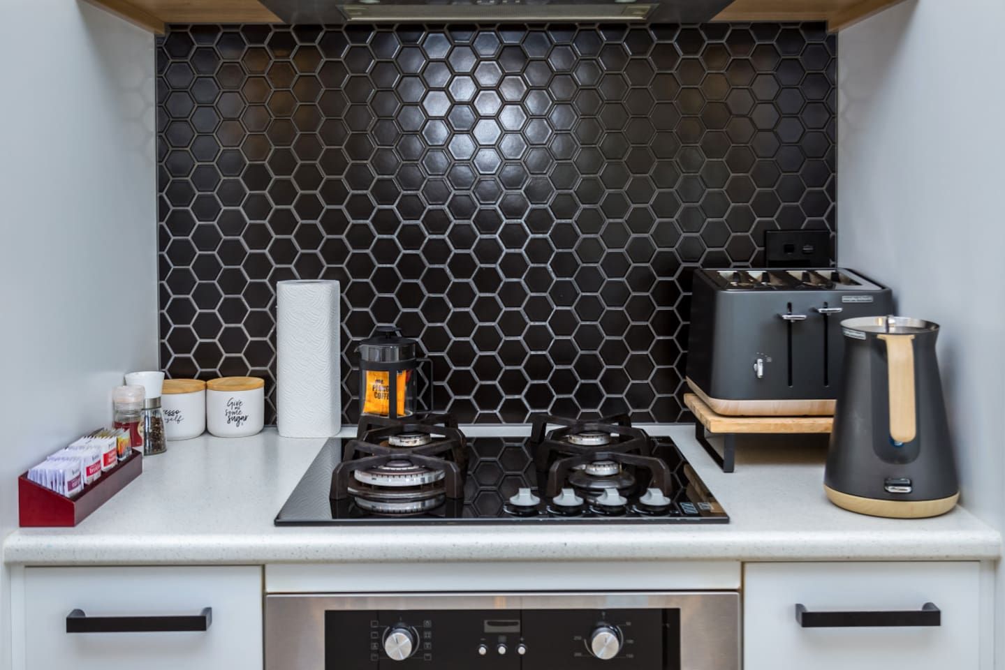 Une cuisine compacte équipée d’une cuisinière à gaz, d’une machine à café et d’une bouilloire.