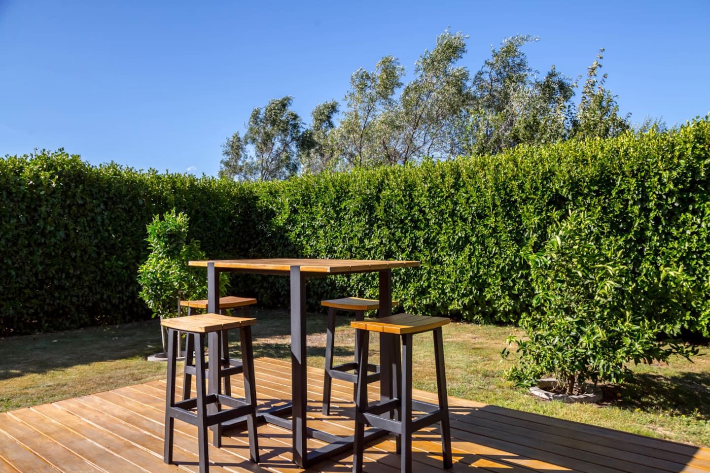 Une terrasse extérieure avec une table en bois et quatre tabourets.