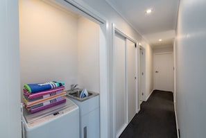 A narrow hallway with a laundry area on the left, featuring a stacked washer and dryer, a sink, and a pile of folded towels. - La Maison Noir, Martinborough (Martinborough)