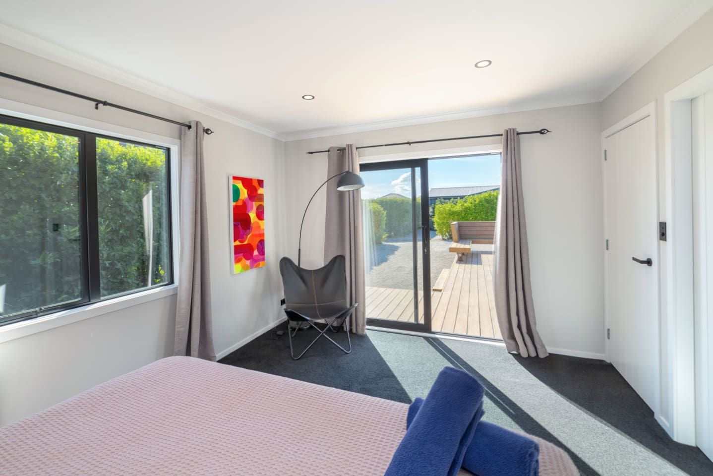 A modern bedroom with a large bed, a chair, and a view of an outdoor deck.