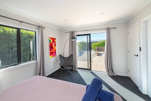 A modern bedroom with a large bed, a chair, and a view of an outdoor deck. - La Maison Noir, Martinborough (Martinborough)